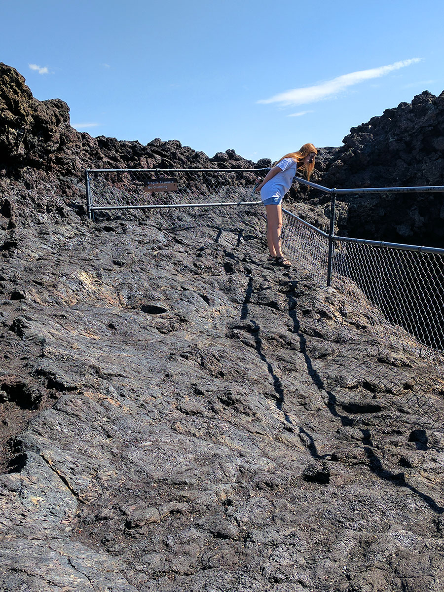 a girl looking down into one of the miniature volcanoes at Craters of the Moon National Monument