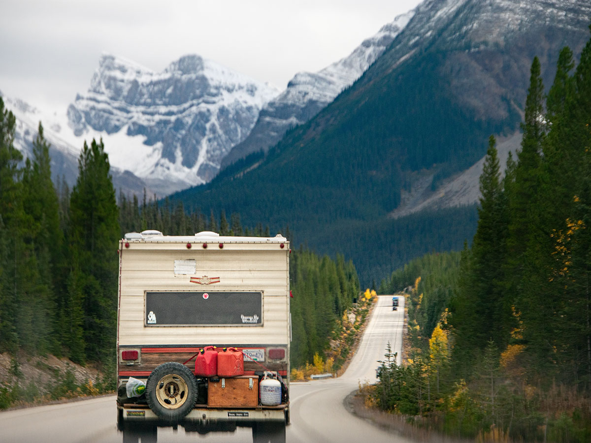a camper on the road surrounded by mountains and trees