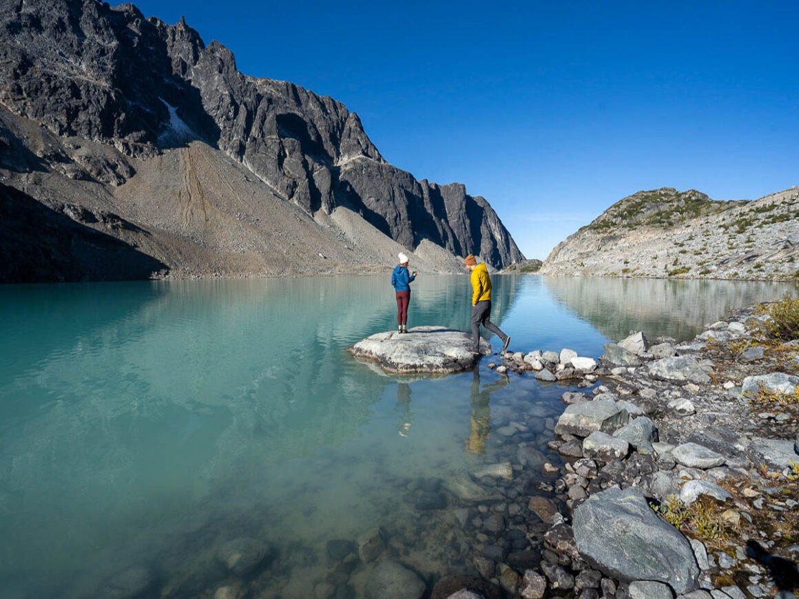 Two people walking on the rocks of a  gorgeous green lake along the Sea to Sky Highway