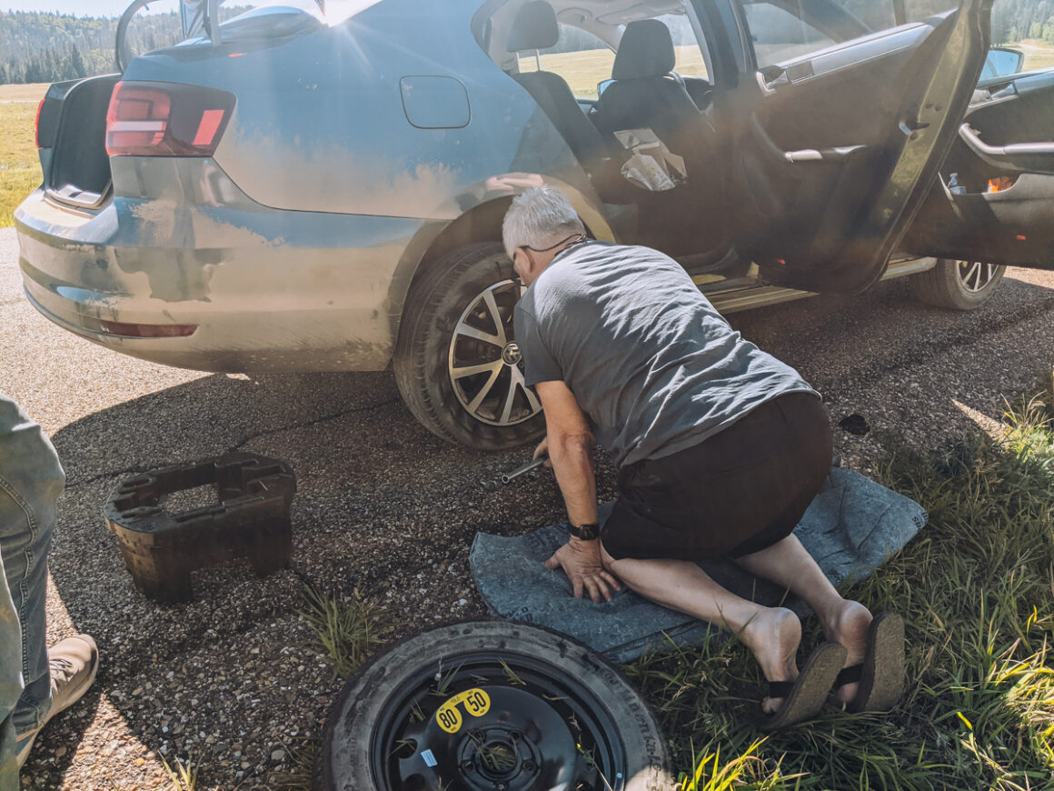 a man changing a flat tire what should I check on my car before a road trip