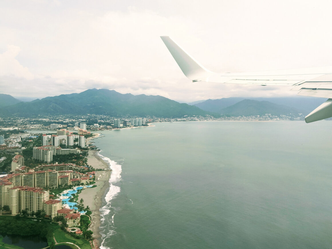 A plane wing over the water and beach of Mexico