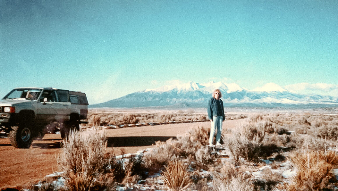 a girl standing beside a raised Toyota truck in front of mountains